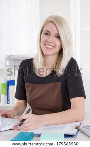 Portrait of young blonde attractive smiling business woman at desk.