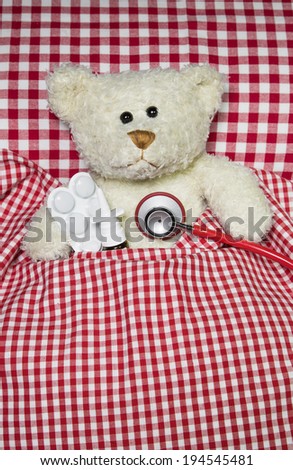Sick teddy bear lying in a red checked bed. Concept for illness.