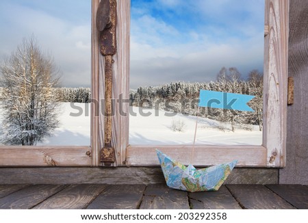 Winter holiday traveller concept: Wooden window sill with sail boat and snowy landscape.