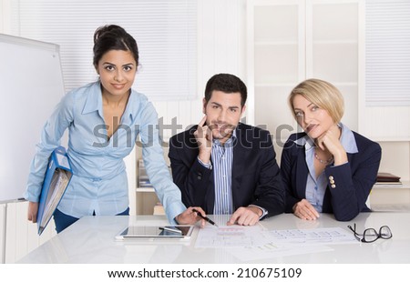 Portrait: successful smiling business team of three people; man and woman in the office wearing commercial blue business outfit.