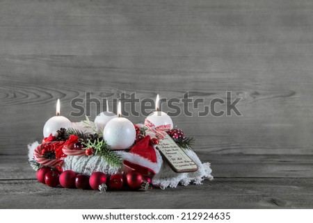 Advent crown with three candles in red and white on grey wooden background.