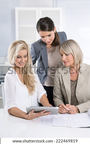 Team: Successful business team of woman in the office talking together looking at tablet computer.