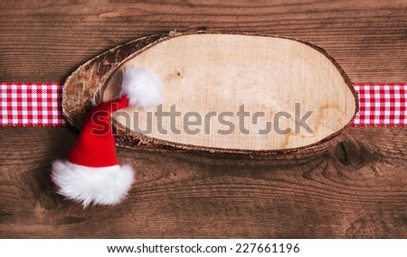 Rustic wooden christmas card or billboard with santa hat and red white checkered bow.