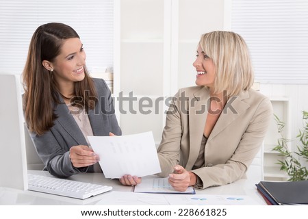 Team: two successful businesswoman sitting at desk having fun at work.
