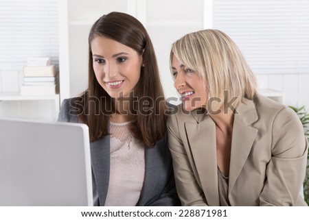 Two smiling attractive businesswoman working in a team looking at screen.