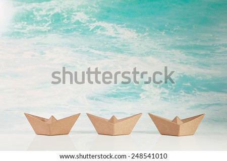 Business concept for challenge and movement: three paper boats on maritime turquoise ocean background.