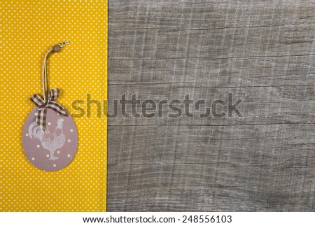 Easter decoration with cock label hanging on a yellow dotted fabric on wooden background.
