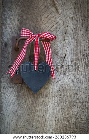 Black heart with a red white checked ribbon hanging on an old door.