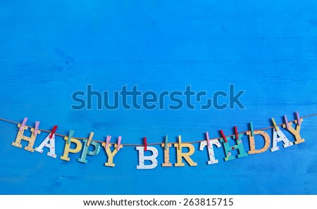Blue background with colorful wooden hanging letters on a clothes line with text: happy birthday.