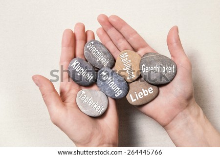 Inner balance concept: hands holding stones with german words for: hope, courage, intelligenz, justice, equality, love and temperance,