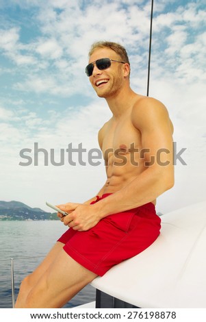 Attractive happy young man or sailor on a sail boat with sun glasses, red shorts and sun glasses.
