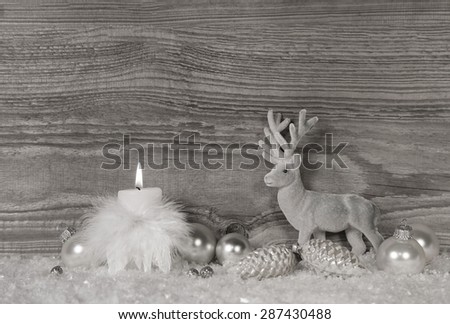 Grey, white silver christmas decoration with one burning candle on wooden background.