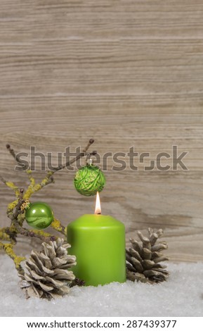 One burning advent candle on an empty wooden background with snow and other decoration.