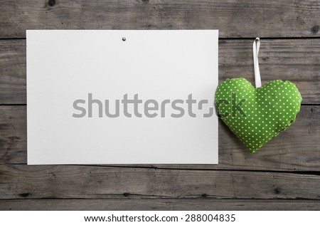 White paper on an old wooden wall with a lime green hanging heart with polka dots for a background.