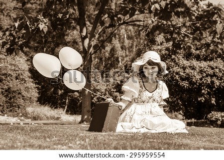 Sad and disappointed young girl sitting with her suitcase alone in the garden.