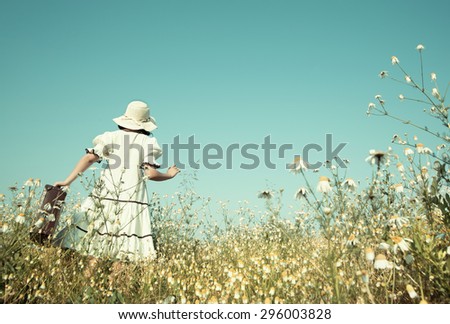 Girl on the way to her future walking in a flowery meadow with her suitcase.