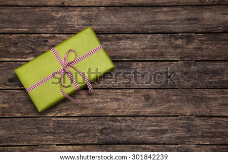 One green gift box wrapped in apple green box with red white checked ribbon on old rustic wooden brown background for christmas.