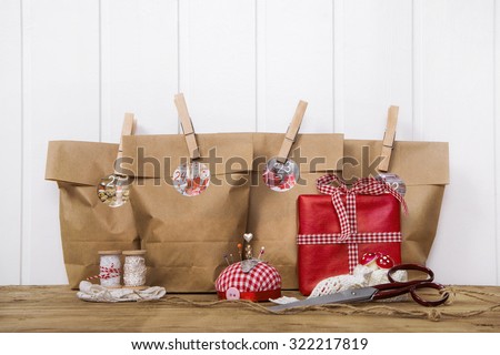 Crafted christmas presents wrapped in paper bags with wooden clips in red and white colors with sewing supplies.