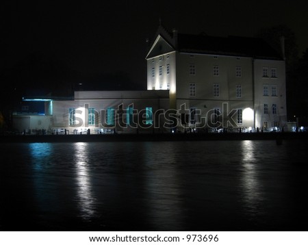 House on river bank with several lights reflecting in water. mucha museum, Prague, kampa