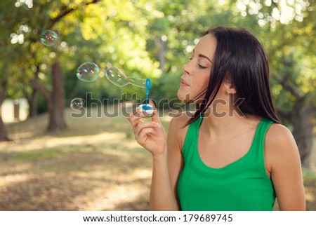 Beautiful young woman blowing soap bubbles outdoors