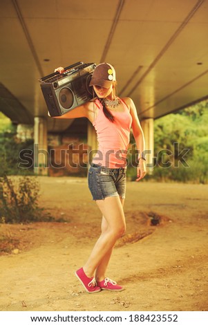 Beautiful hip hop woman with a cap which holding a tape recorder on shoulder