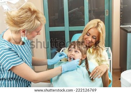 Little girl sitting in mom\'s lap while dentist examines her teeth