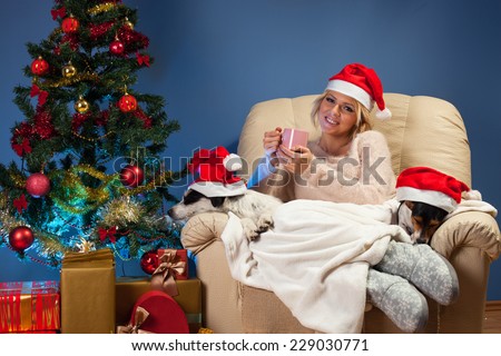 Beautiful young woman sitting near Christmas tree in a armchair with two dogs and drinking tea