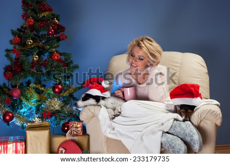 Beautiful young woman sitting near Christmas tree in a armchair with two dogs and drinking tea