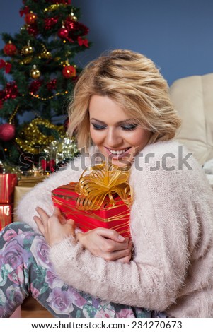 Beautiful young woman sitting near Christmas tree and holding a gift in arms