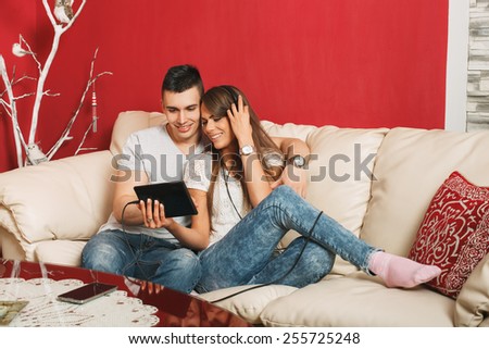 Young couple sharing music on digital tablet in sofa at home