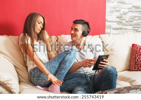 Young couple sharing music on digital tablet in sofa at home