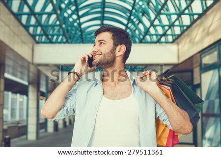 Young man using phone and holding shopping bags