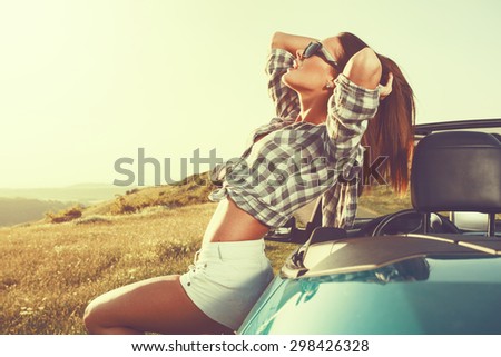 Attractive young woman posing leaning on convertible car at sunset