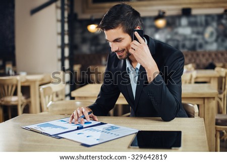 Businessman sitting at table in cafe and talking on mobile phone.