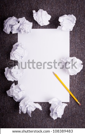 Crumpled and wrinkled white paper wads with fresh sheet of blank paper over dark texture