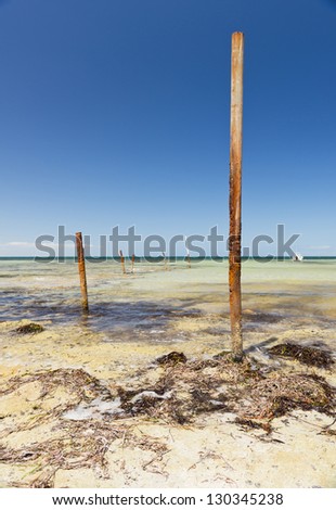 Rusting metal poles stick out of the ocean with blue sky behind