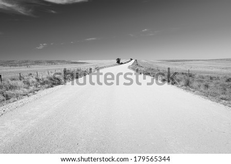 Dirt road in country Australia stretches into the distance under a blue sky in black and white