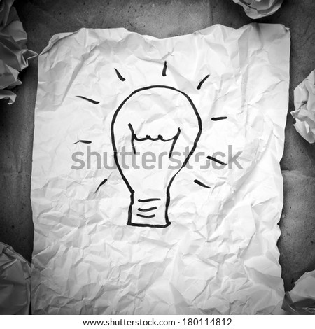 Crumpled paper with a lightbulb idea concept and crumpled paper attempts around it in black and white