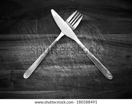 Stainless steel cutlery knife and fork on a wooden chopping board in black and white