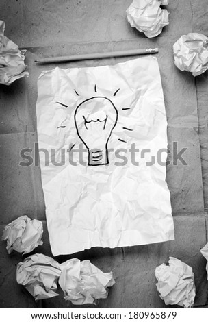 Crumpled paper with a lightbulb idea concept and crumpled paper attempts around it in black and white