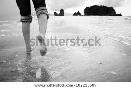 A young woman walks alone on a beach in black and white