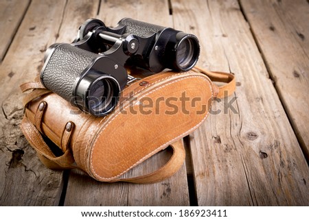 Pair of old binoculars with vintage leather strap and case on a rough wooden surface