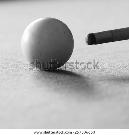 Pool cue and the white ball in shallow focus on a pool table in black and white
