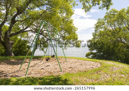 Playground equipment swings for children next to the sea, under huge trees