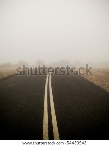 Dark road with double lines disappears into very thick fog