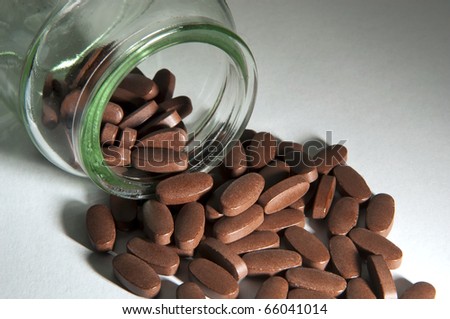 Generic pills spill out of a clear glass bottle