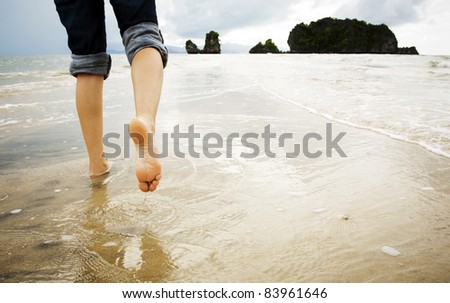 A young woman walks alone on a beach, just her feet and legs showing
