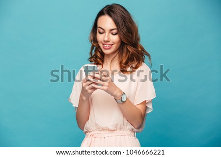 Contented smiling woman typing text message or scrolling through social networks using smartphone isolated over blue background