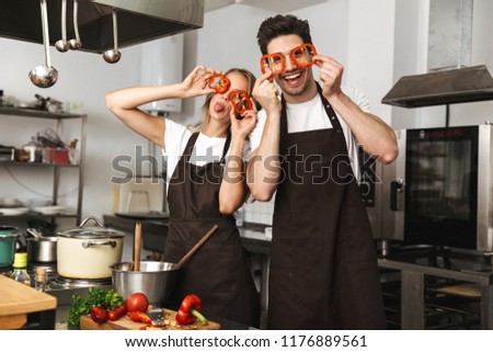 Image of smiling excited young friends loving couple chefs on the kitchen cooking having fun covering eyes with paprika.