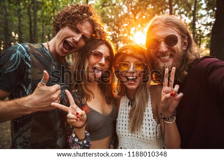Photo of joyful hippie people men and women smiling and taking selfie in forest